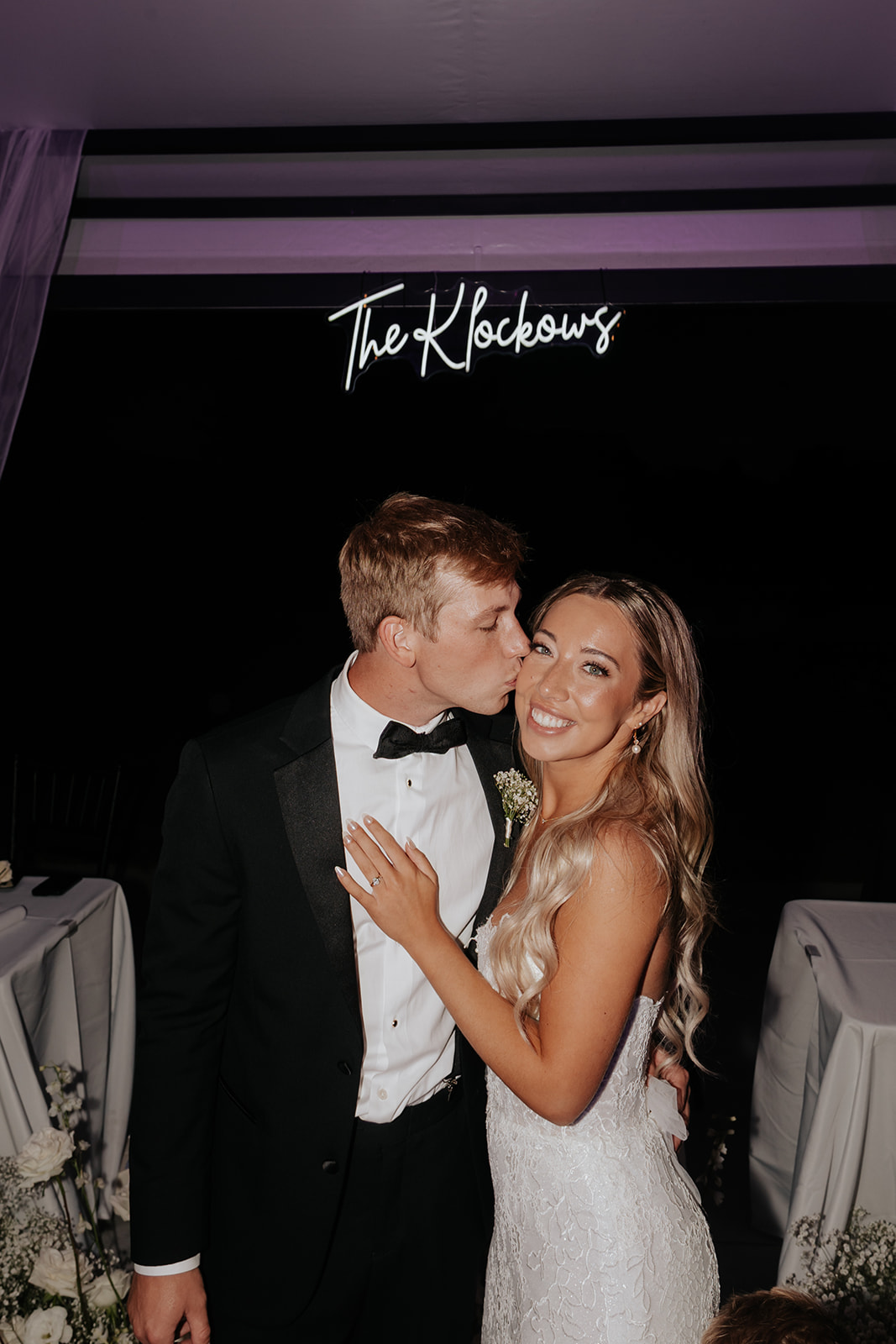 Grant kisses Lauren's cheek beneath the glowing neon The Klockows sign at night