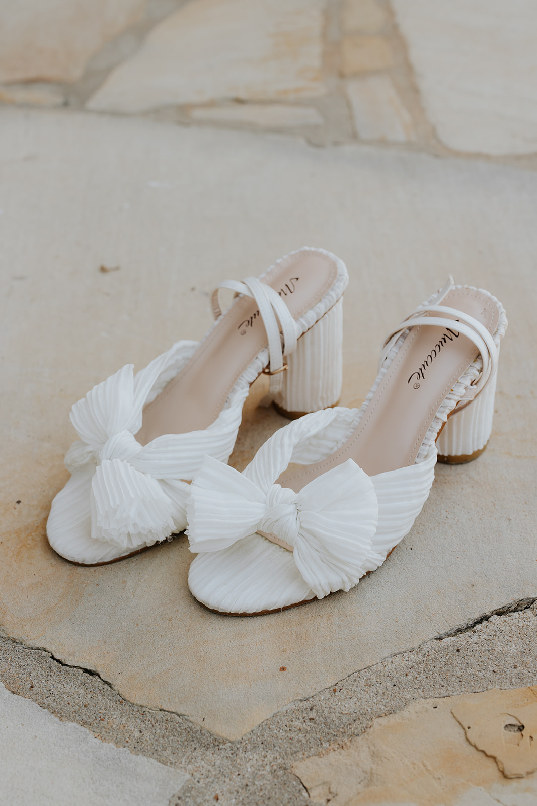 White pleated bow block heels resting on a stone step, ready for the wedding morning