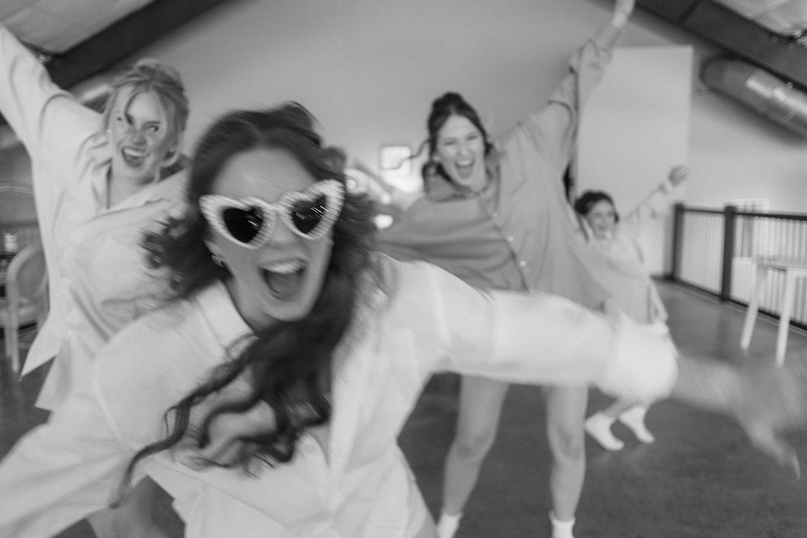 Black and white of the bride in heart sunglasses dancing with her bridesmaids before the ceremony