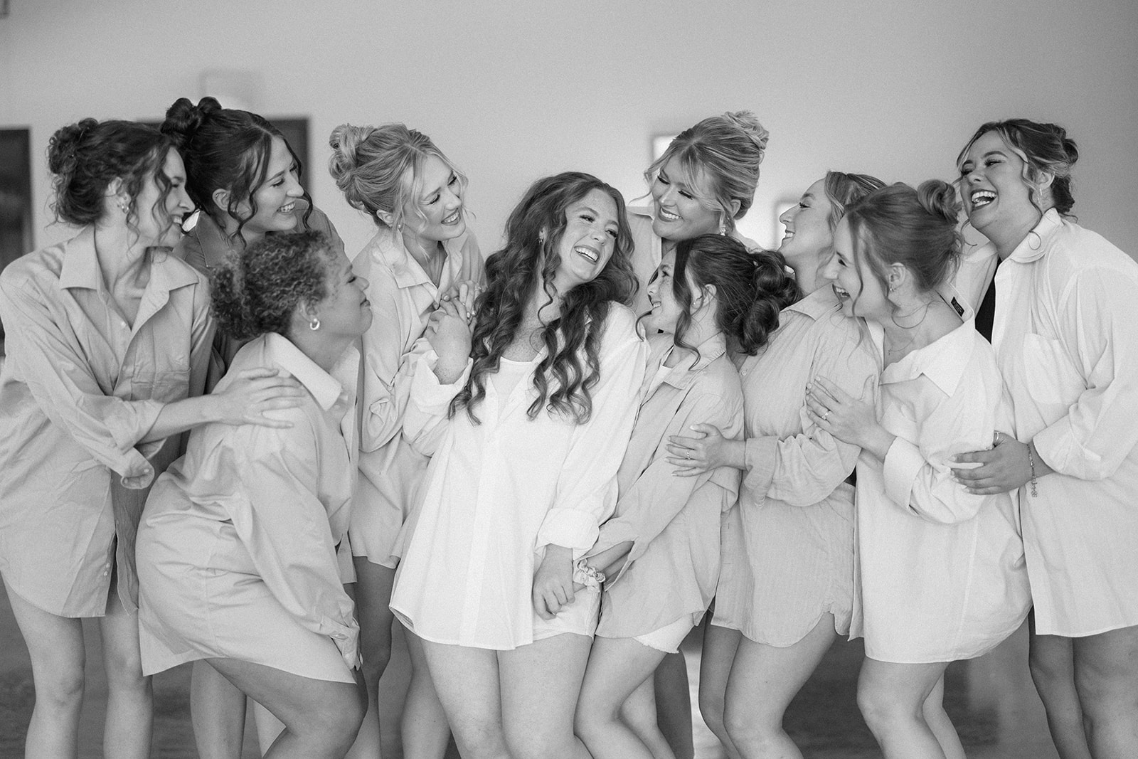 Black and white of the bride and her bridesmaids laughing together in matching getting-ready shirts