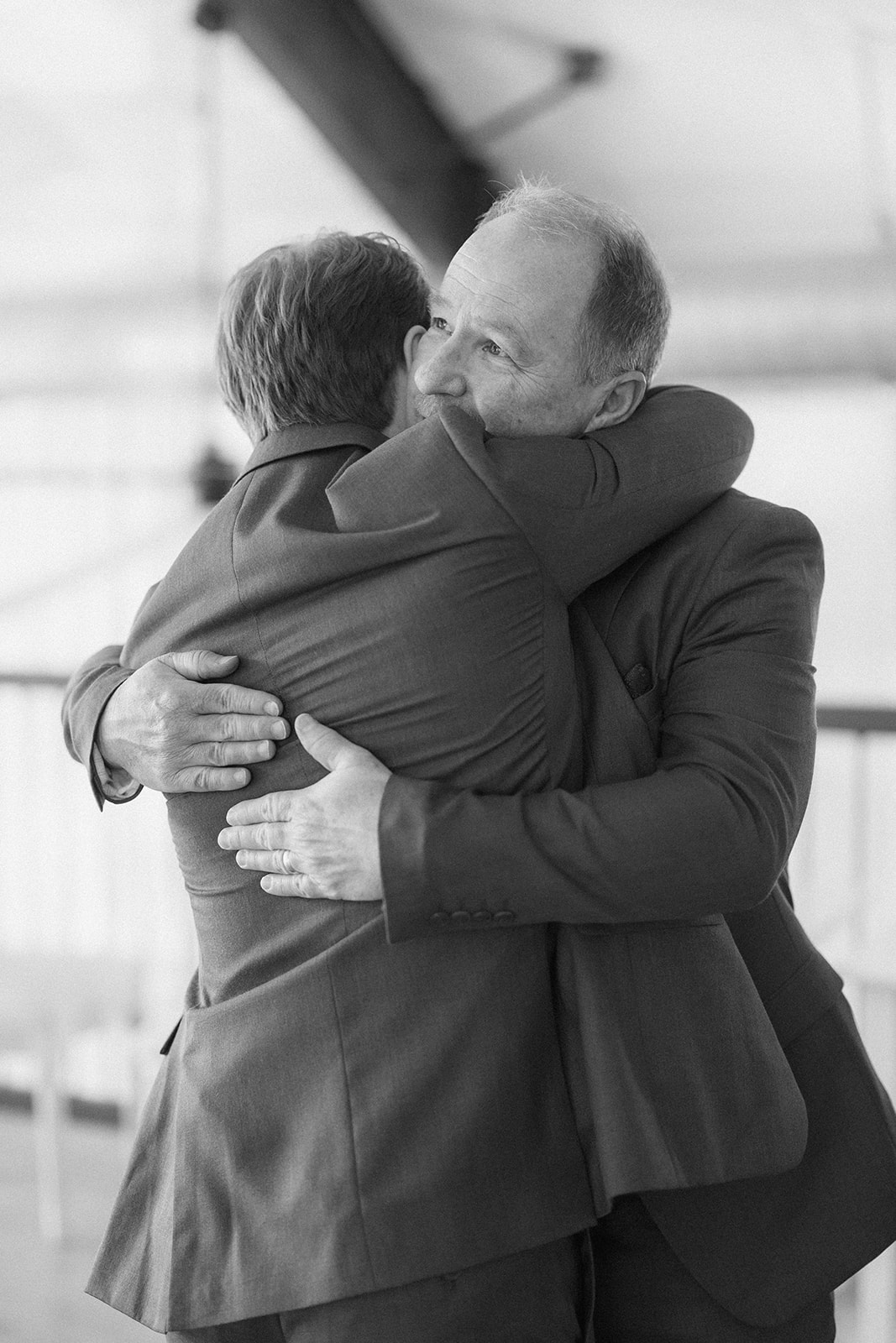 Black and white of the groom sharing a long hug with an older man before the ceremony