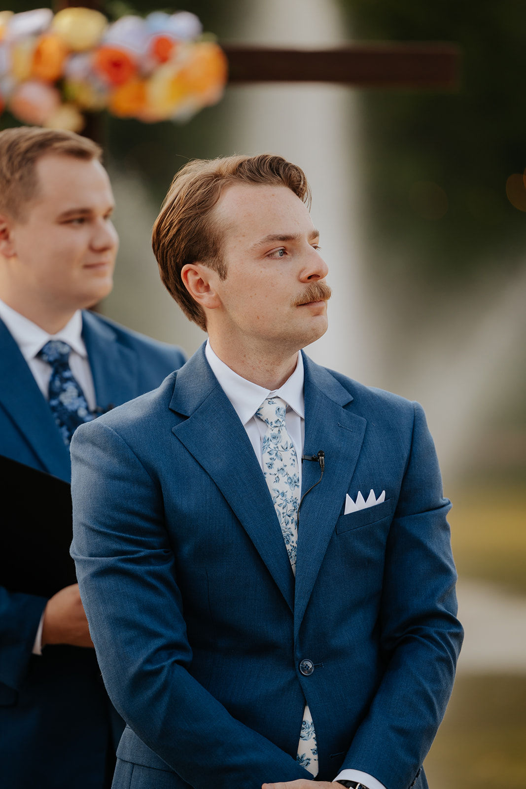 The groom in a blue suit watches the bride come down the aisle