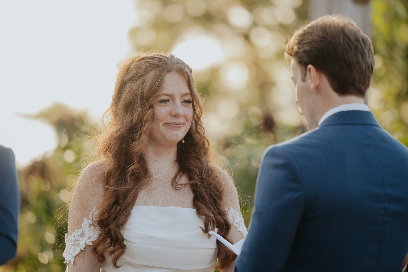 The bride smiles through tears as she listens to the groom's vows at golden hour