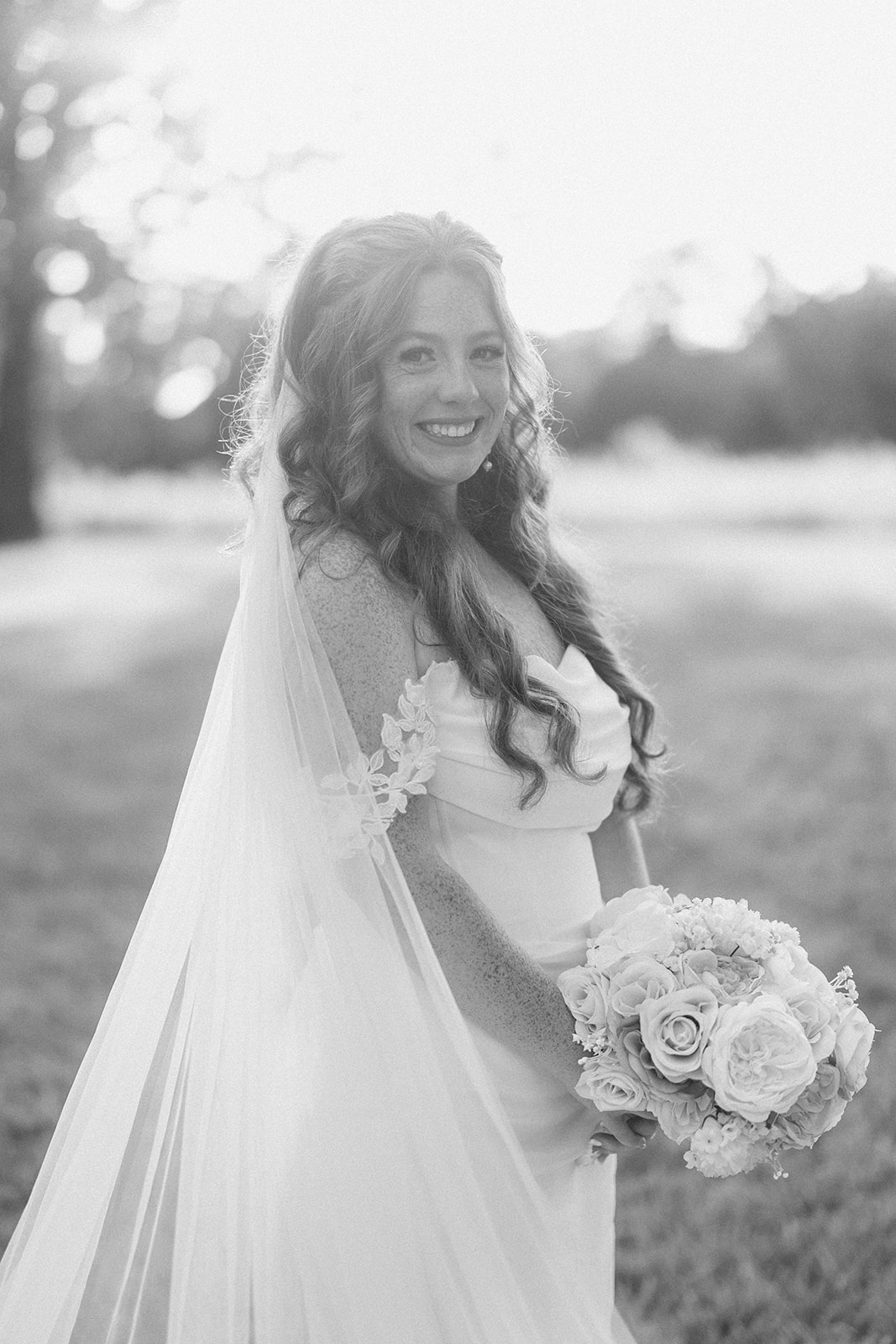 Black and white portrait of the bride in her long veil holding a white rose bouquet
