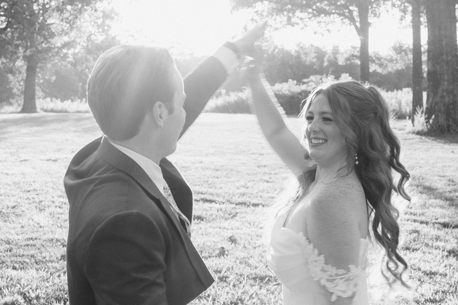 Black and white of the groom twirling the bride in a sunlit field