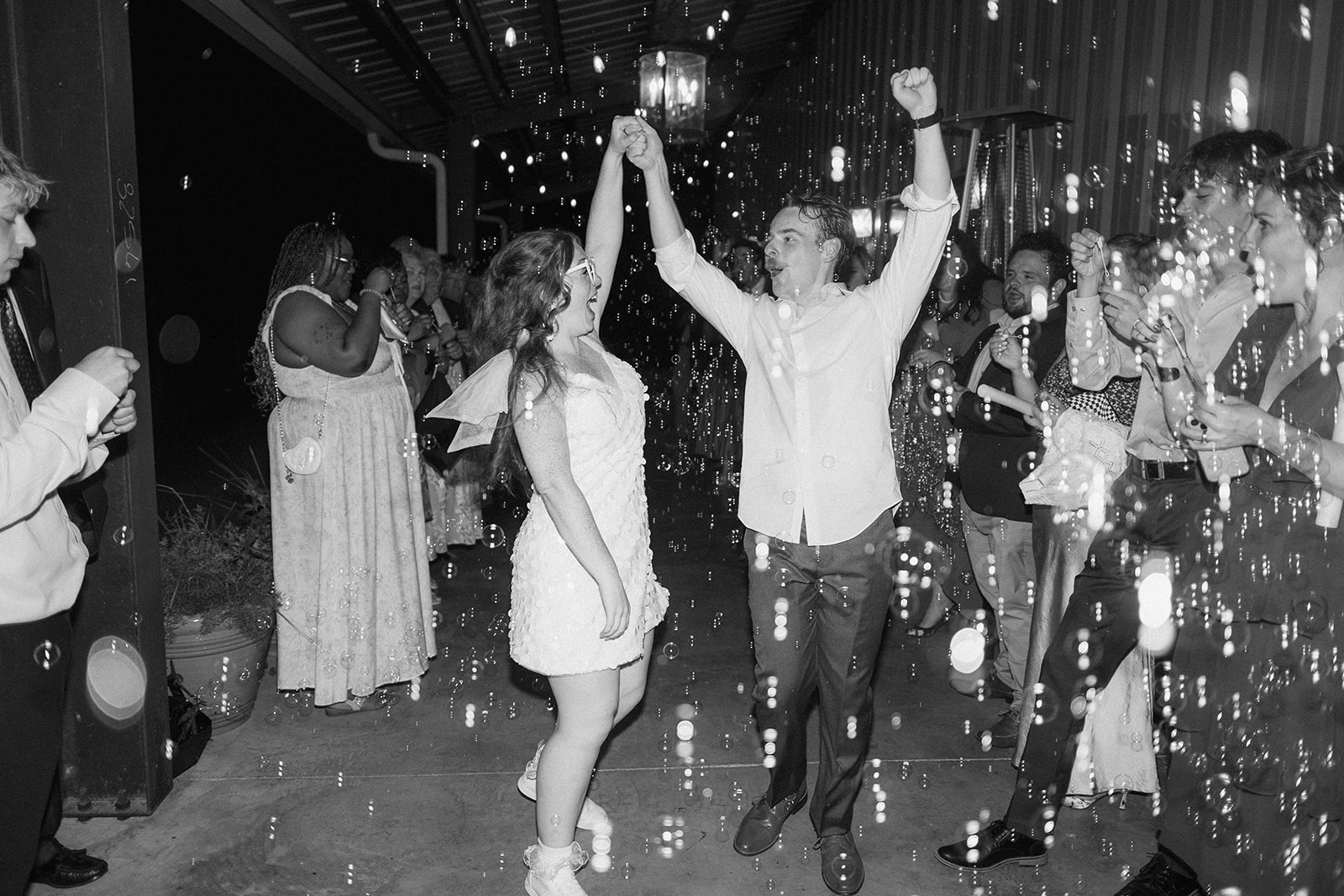 Black and white of Maci and Matt cheering under a shower of bubbles during their send-off