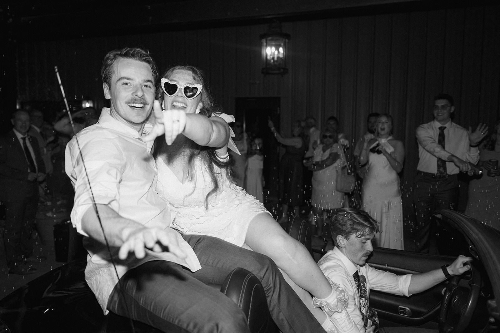 Black and white of Maci and Matt riding out in a golf cart, the bride in heart sunglasses