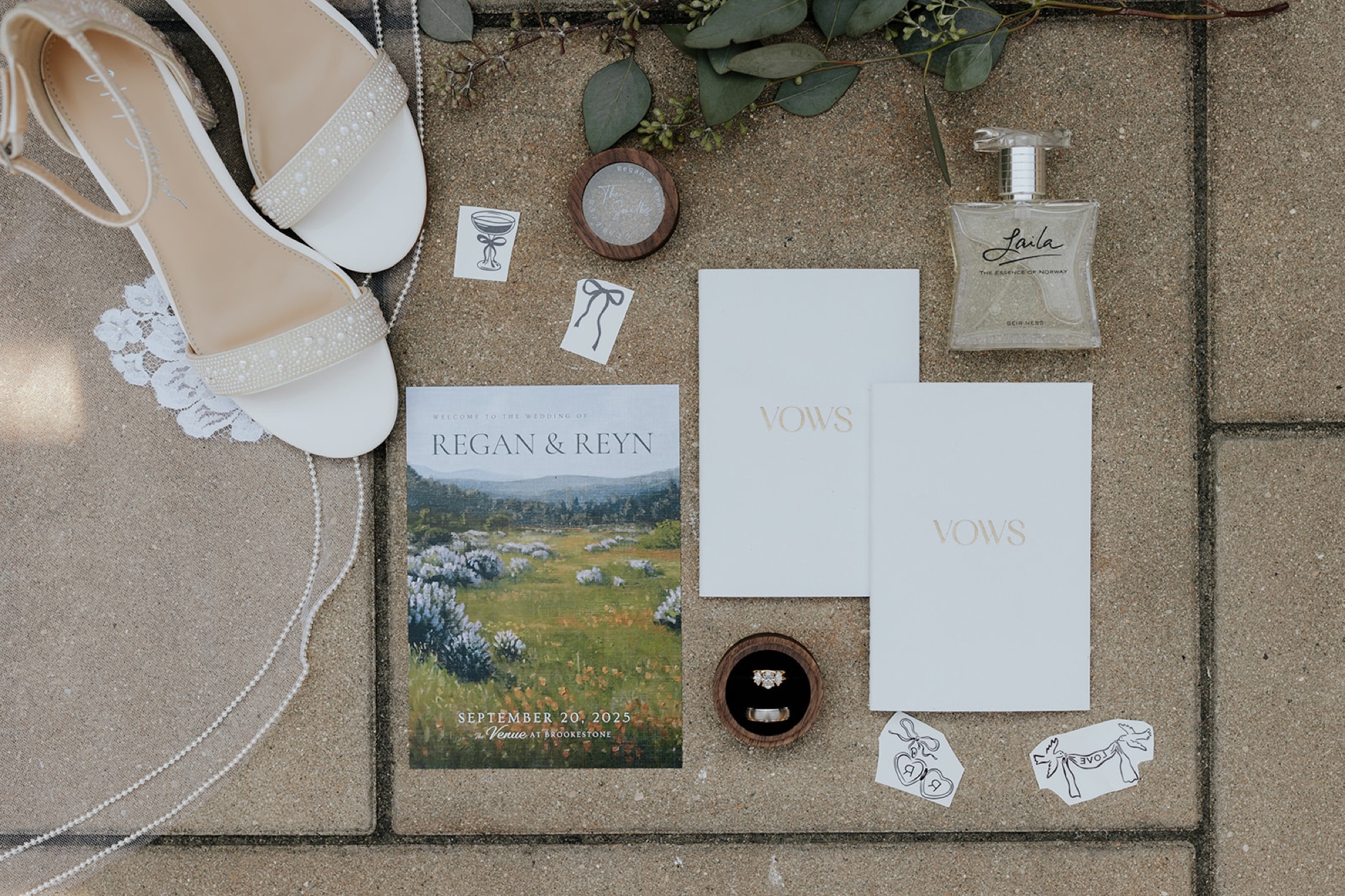 Flat lay of the Regan and Reyn invitation suite, vow books, rings and bridal heels