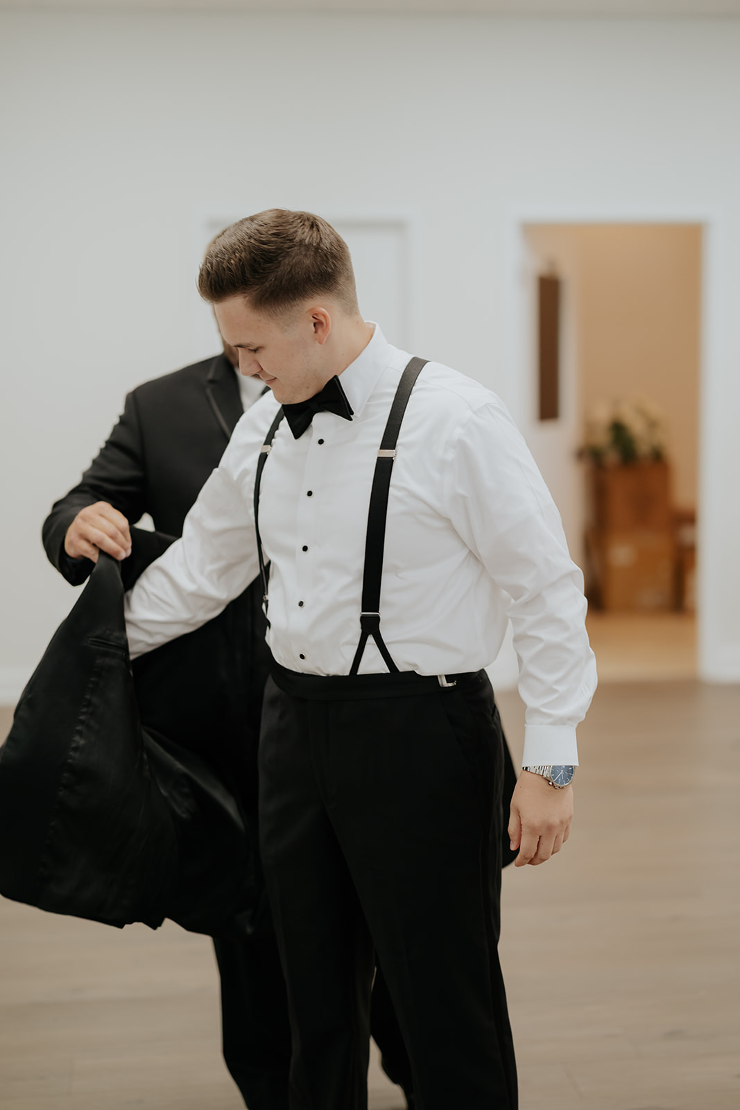 The groom pulls on his tuxedo jacket with help from a groomsman