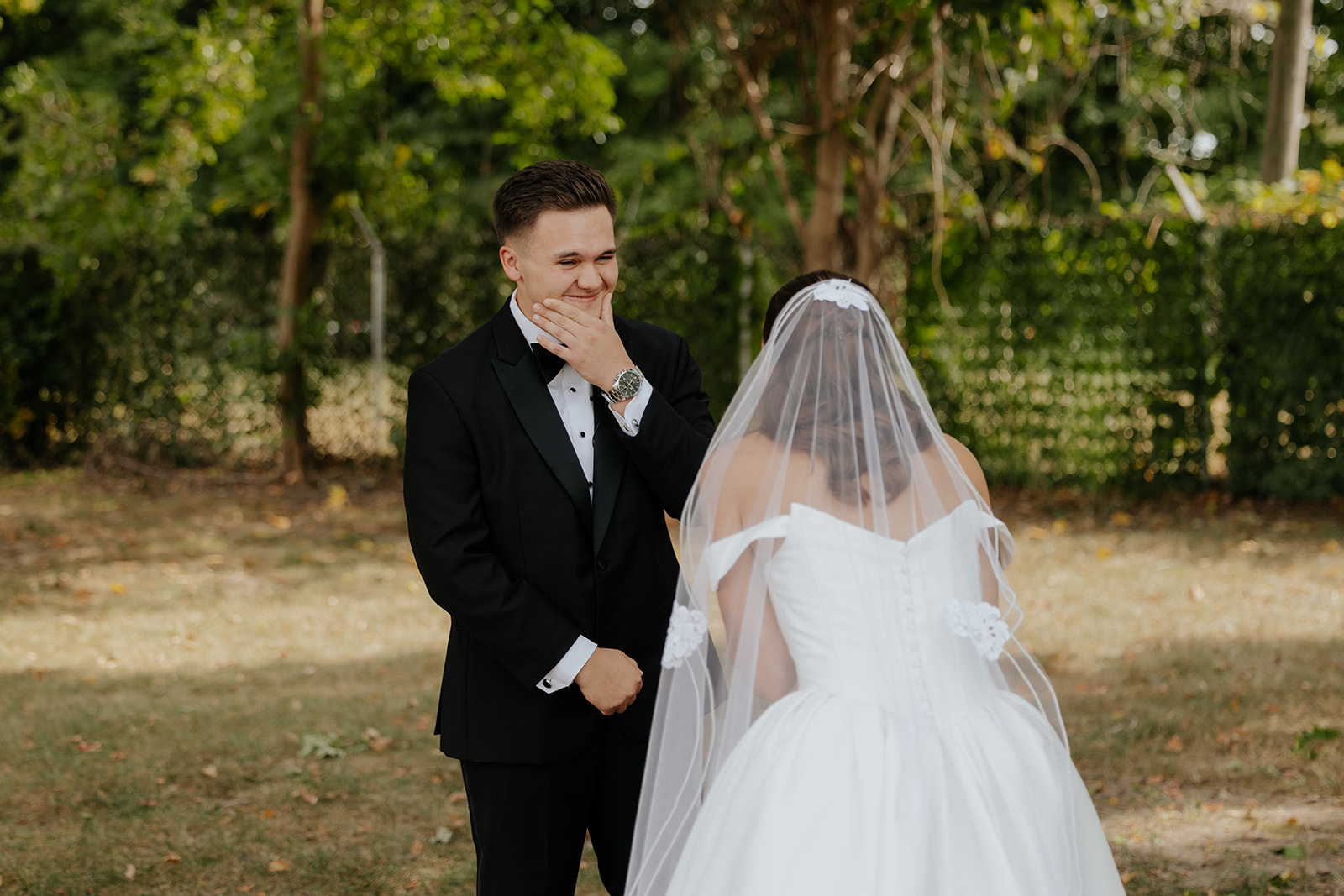 The groom covers his mouth, overcome, as he sees the bride in her veil