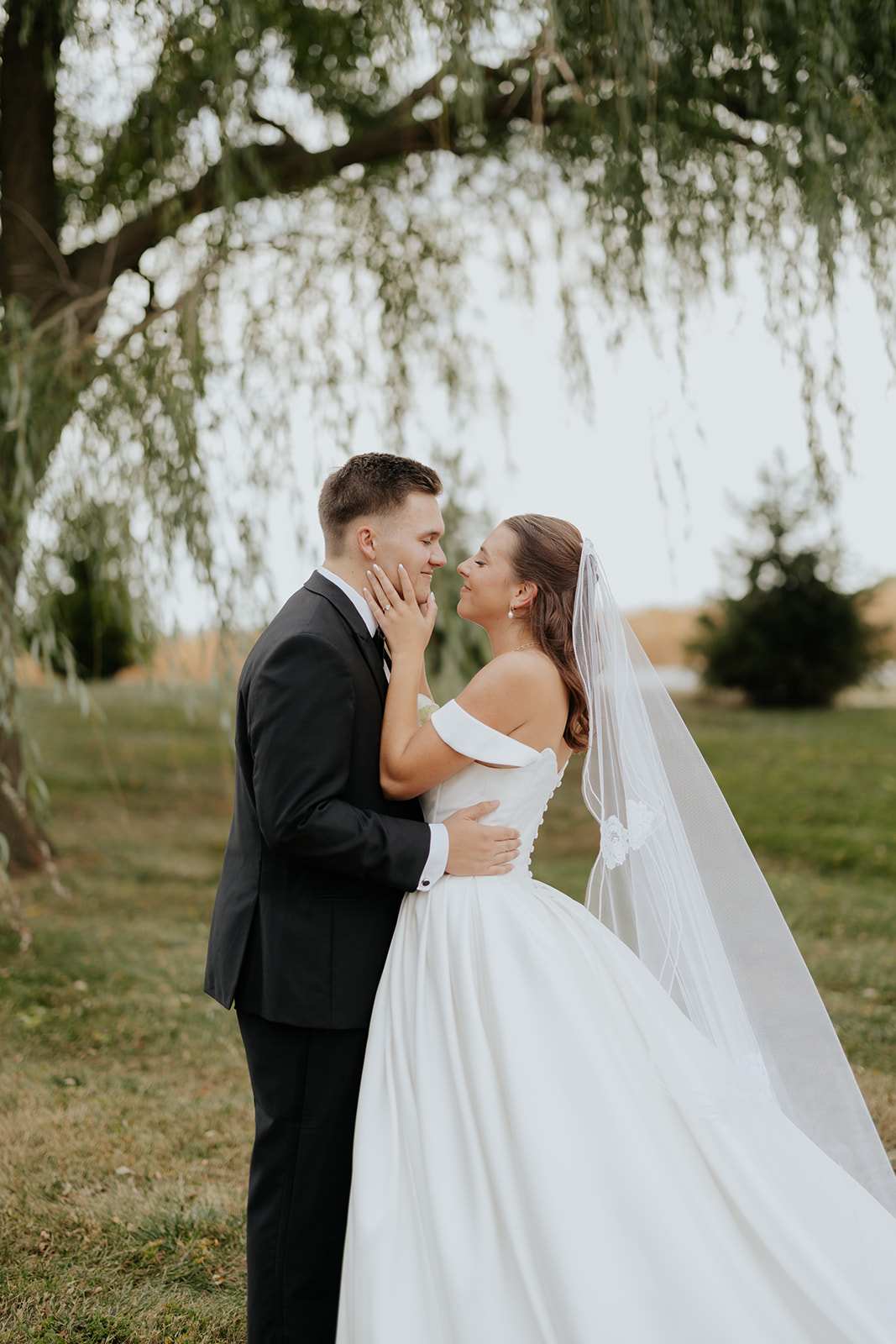 The bride holds the groom's face as they lean in for a kiss in the grass