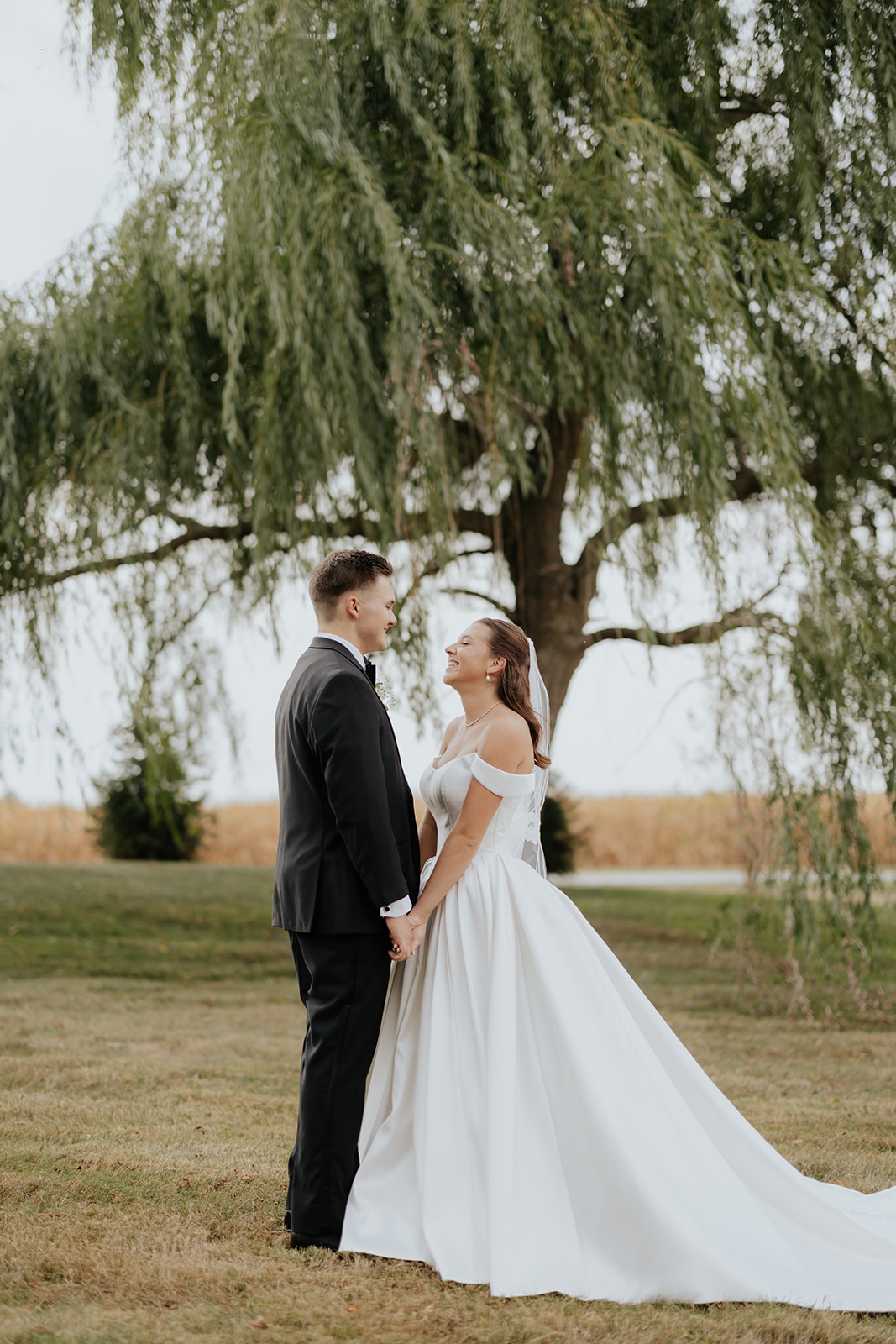 Regan and Reyn embrace beneath the willow tree at The Venue at Brookstone, her train spread on the lawn