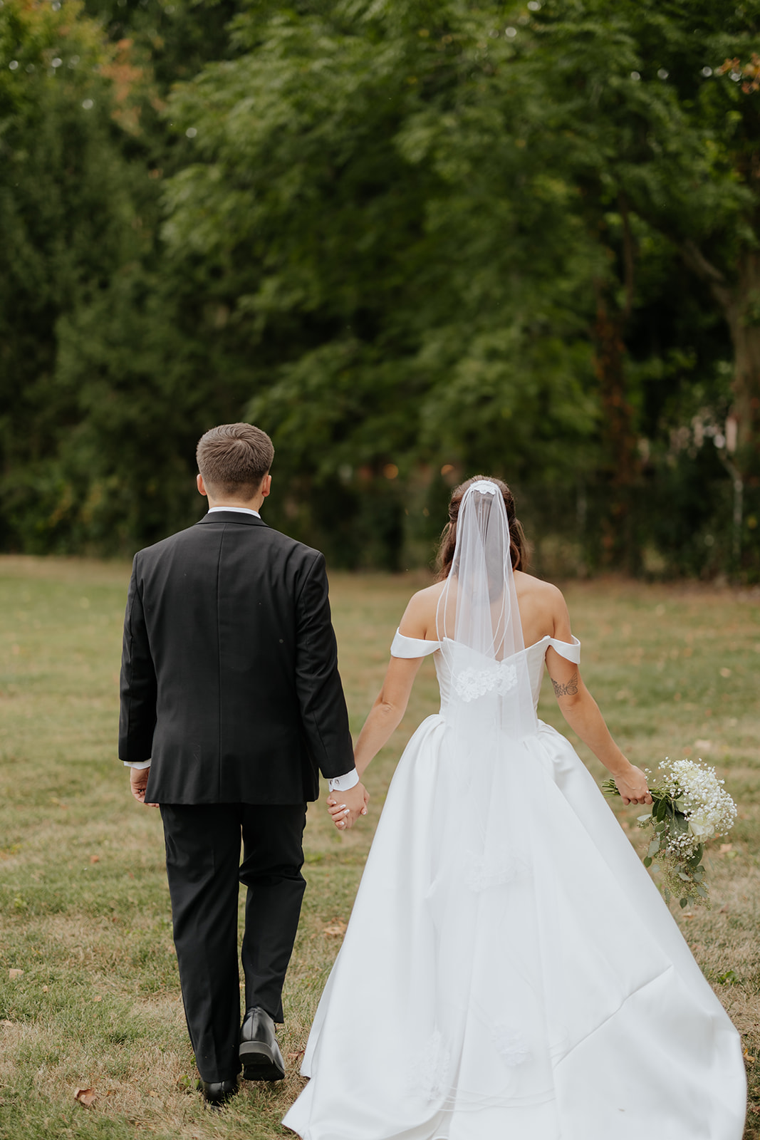 Regan and Reyn walk hand in hand across the lawn toward the trees