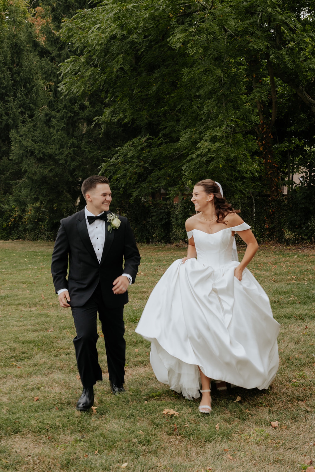 Regan and Reyn laugh as they walk across the grass, the bride lifting her gown
