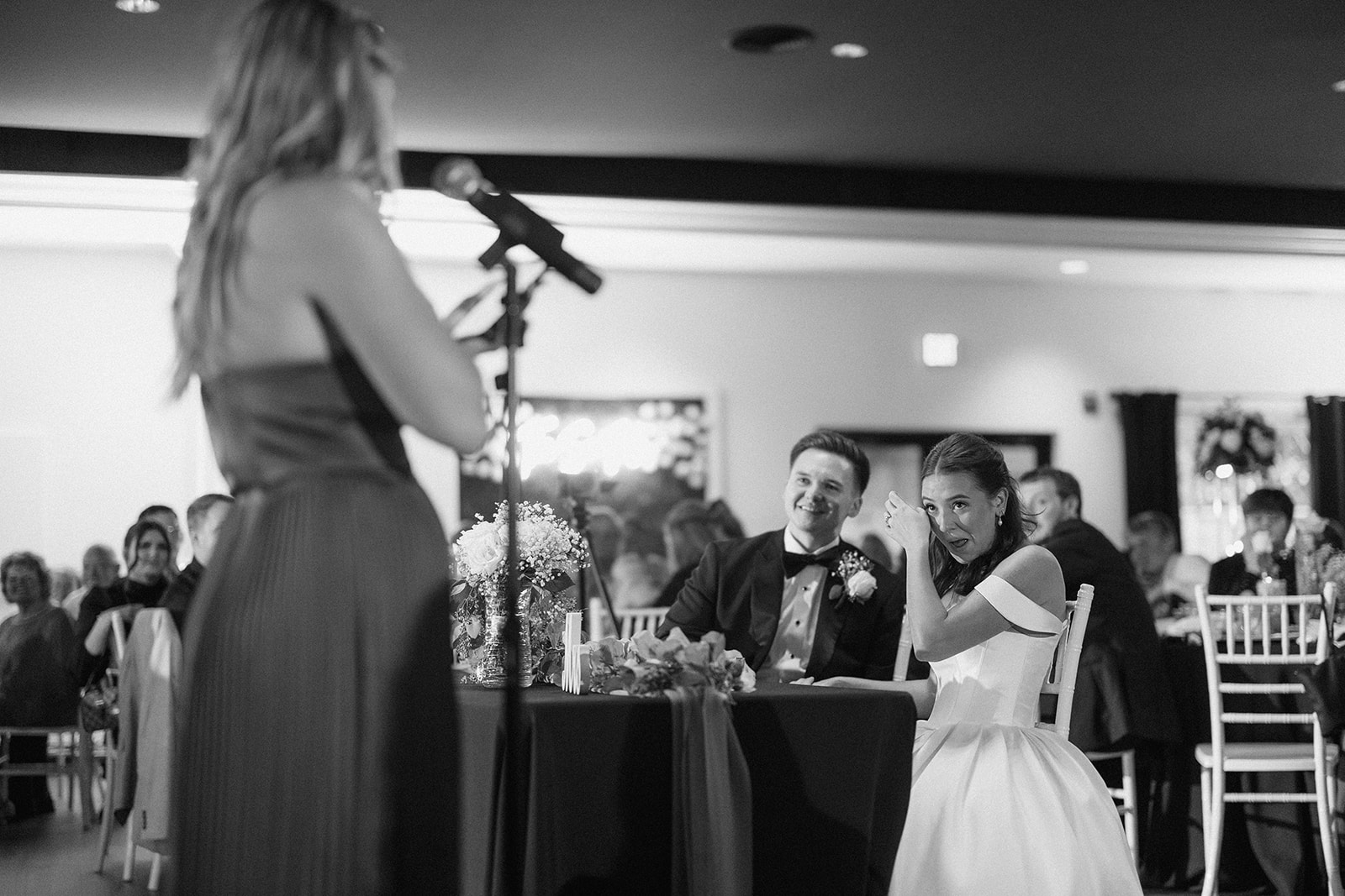 Black and white of the bride laughing at the head table during a bridesmaid's toast